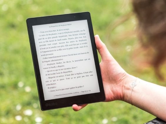 image of a kobo ereader being held out in a grass field.