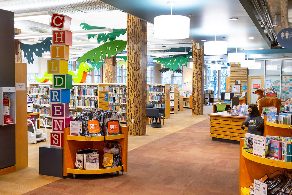 Wide angle shot of the children's section of a library which features shelves of books and pillars decorated as trees.