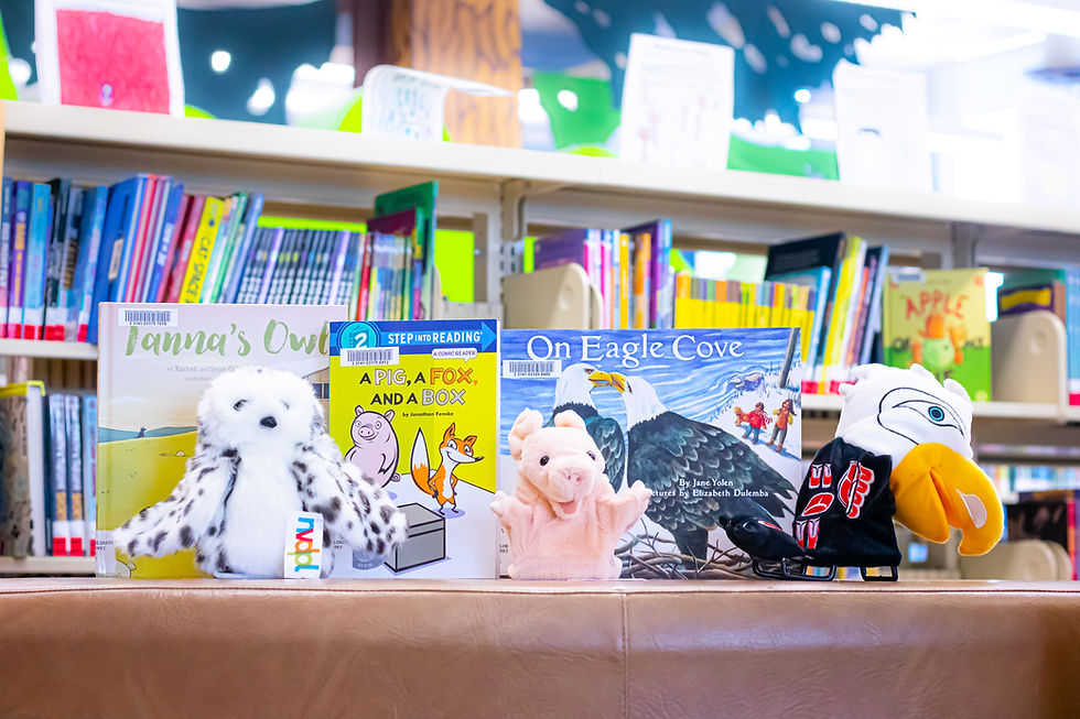 Books and puppets arranged on top of a bookcase. There are three puppets and three kid's books in front of a larger bookshelf of books.