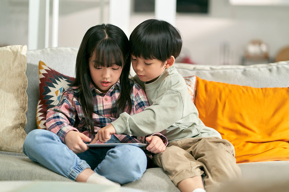 Two children on a couch. One is holding a tablet and the other is reading over the touch the tablet.