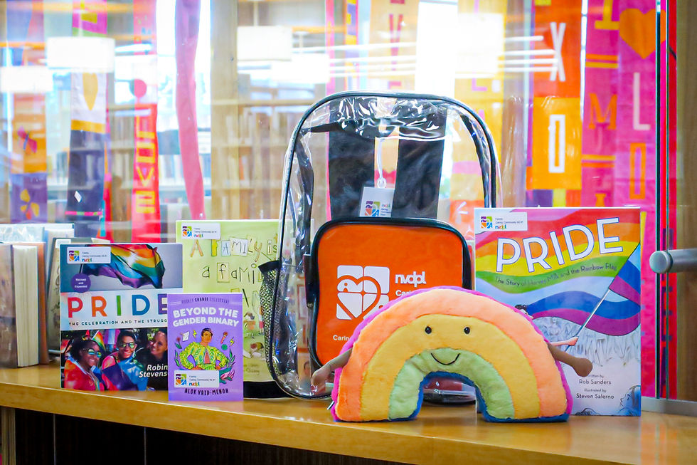 A collection of Pride items including a rainbow plush, four books, and a clear backpack whose contents are hidden by the plush.