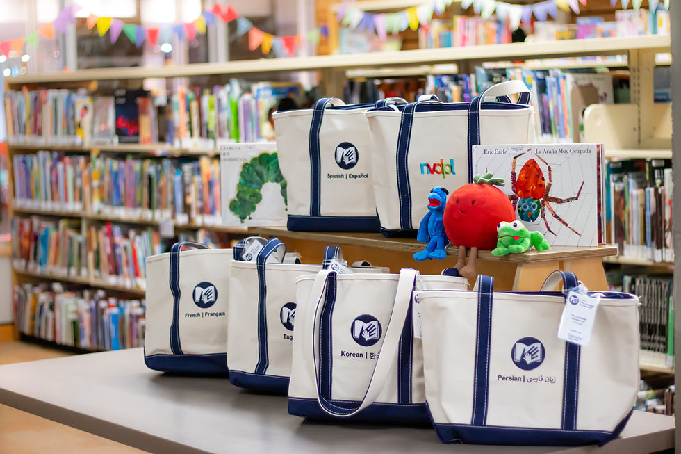 A arrangement of canvas totebags with different languages embroidered on them.  There are also colourful plushies and two childrens book with a spider and a caterpiller.