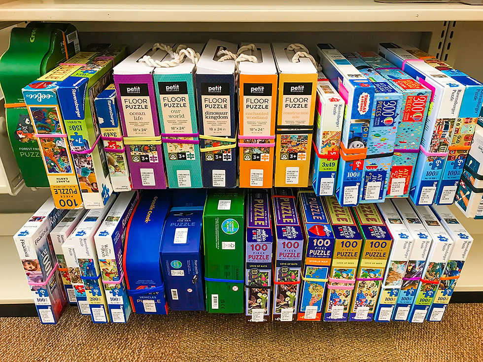 A collection of puzzles of different patterns and difference piece count arranged neatly on two rows of sheves.