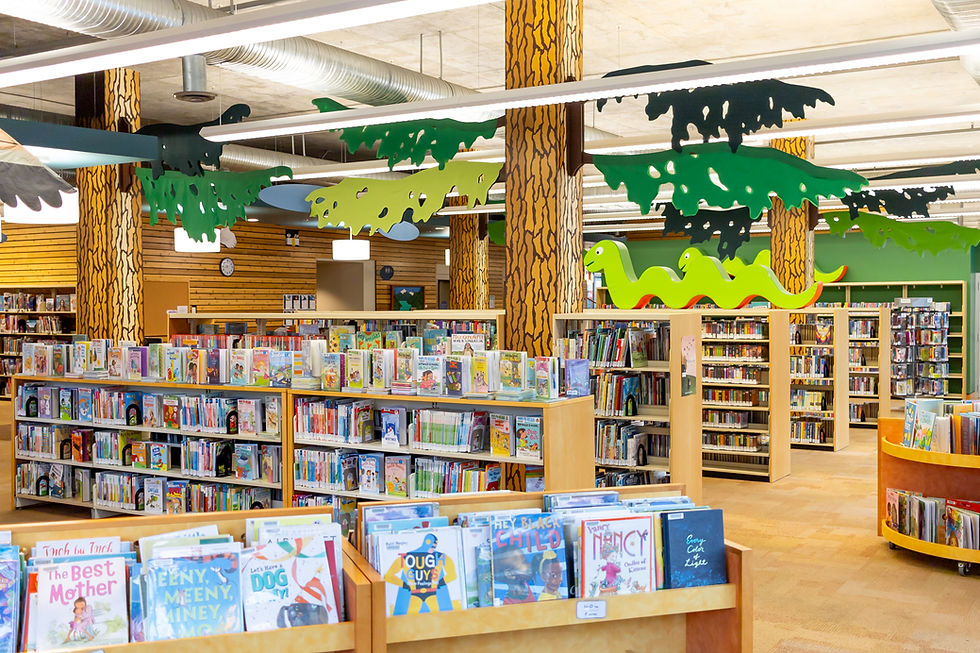 A section of the children's section of the library. There are colourful books displayed on top of a short shelf.