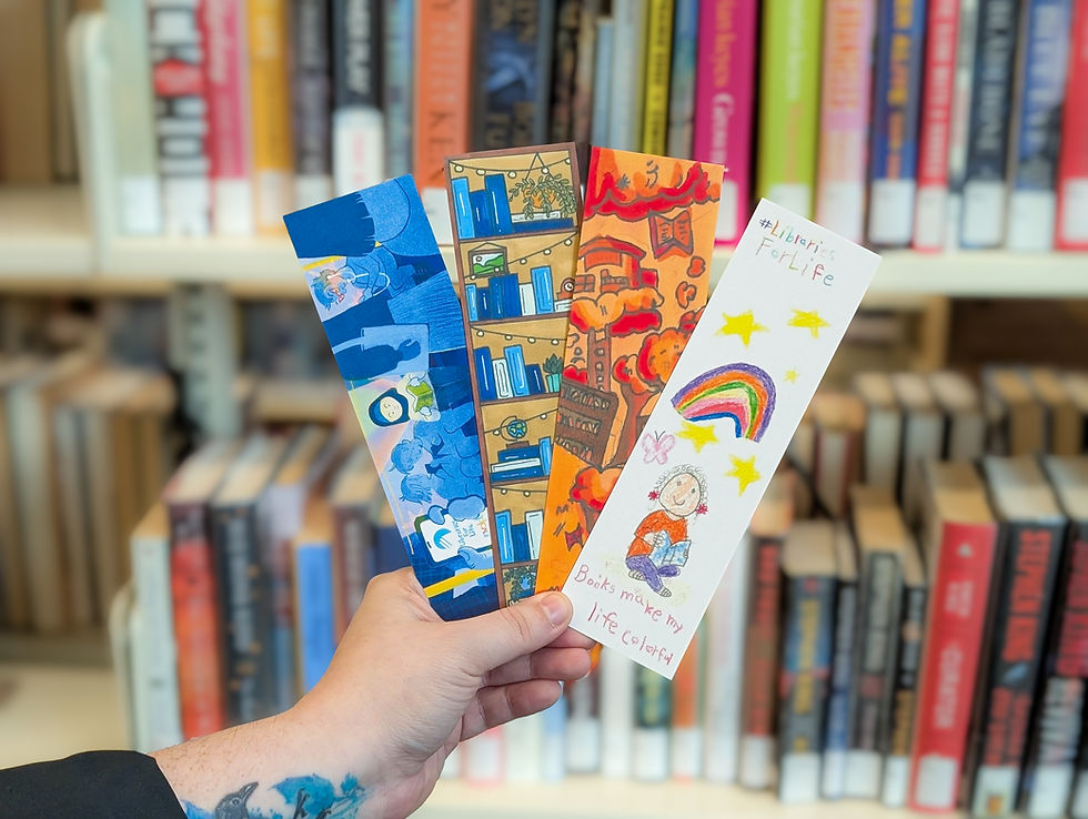 A hand holding 4 bookmarks with various library art designs in front of shelves of books.
