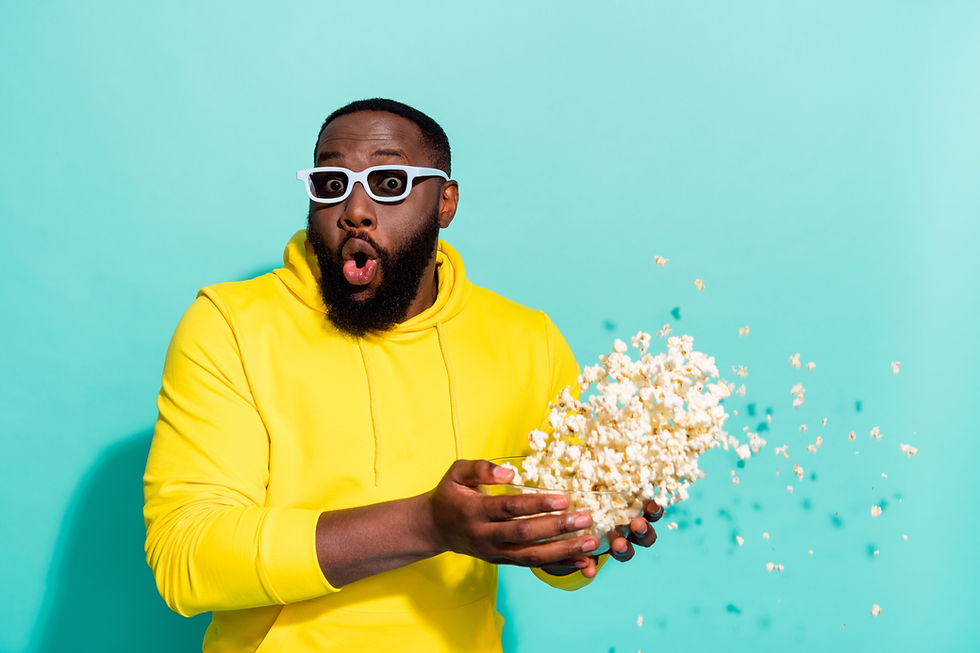 A man wearing a yellow hoodie and sunglasses witha surprised expression throwing popcorn in the air.