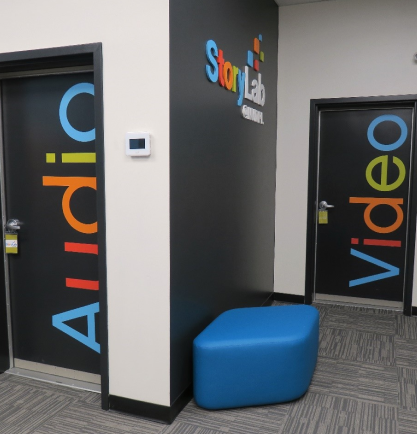 A corner of the StoryLab with the words "audio" on on door and "video" on another. A wall is visible with the StoryLab logo up high and a blue bench by the floor.