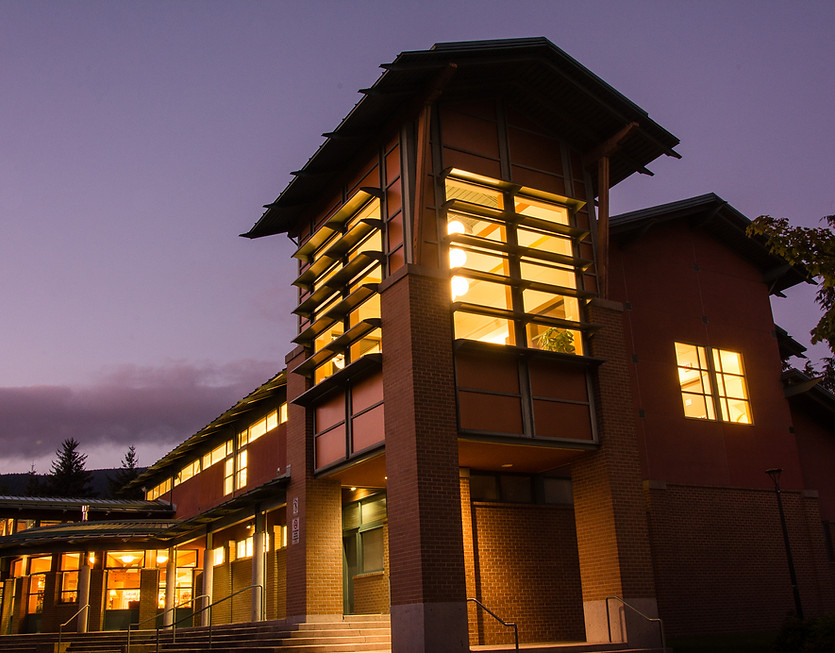 A picture of Parkgate Library's exterior, featuring the "Lantern Room" on the 2nd floor. Light shines from inside the library at dusk. A purple sky can be seen behind.