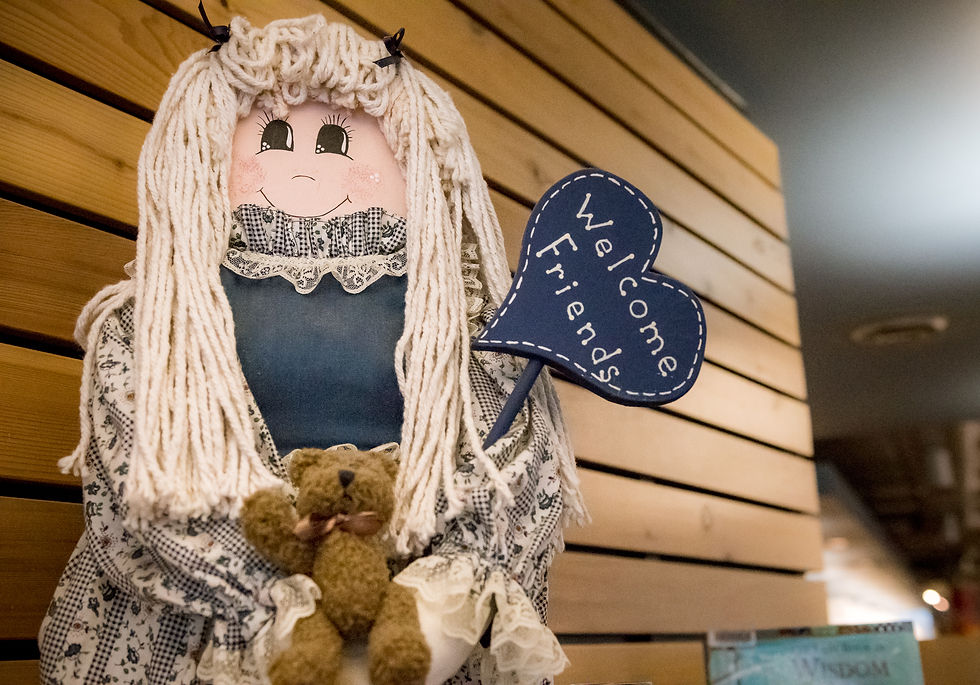 An artisan wooden doll holds a library sign that says "Welcome Friends" in the library.