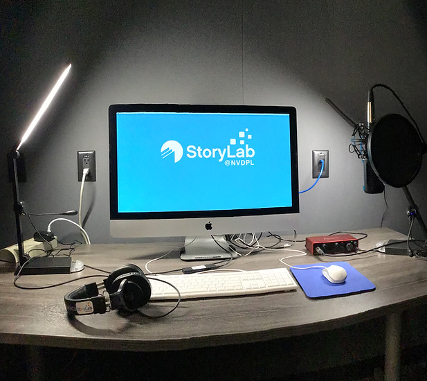 A table with audio recording equipment . There is a computer turned on with a screen displaying the storylab logo on a blue background.